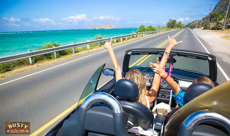 Open top car driving coast road with passengers having fun